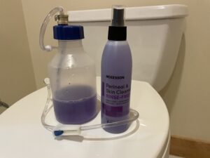 A bottle of liquid and spray on top of the toilet.